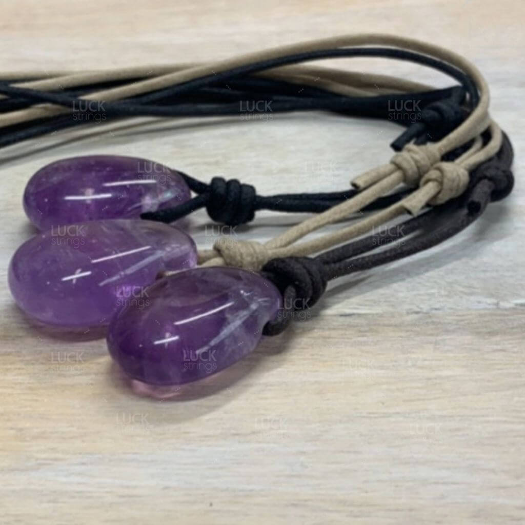 Trio of Luck Strings Amethyst pendants with black, brown, and tan cords laid out, displaying the variety of cord color options.