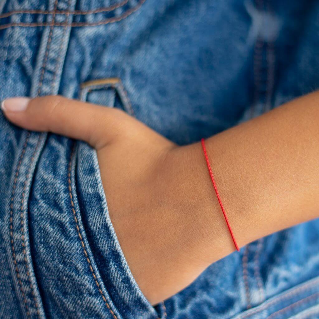 Person pointing at a red string bracelet worn on the wrist - Luck Strings