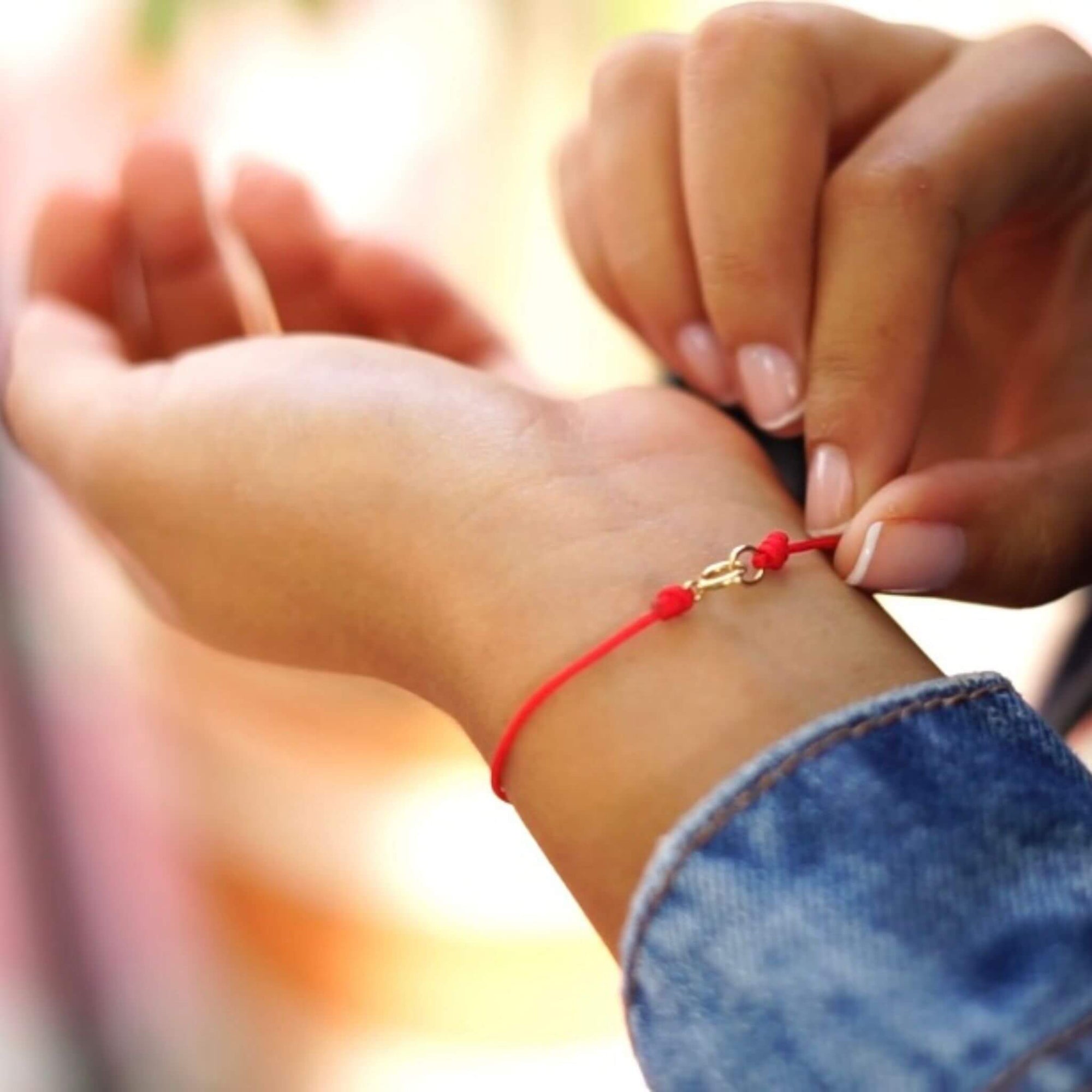 Person wearing a classic red string bracelet with a 14K solid gold clasp on their wrist - Luck Strings
