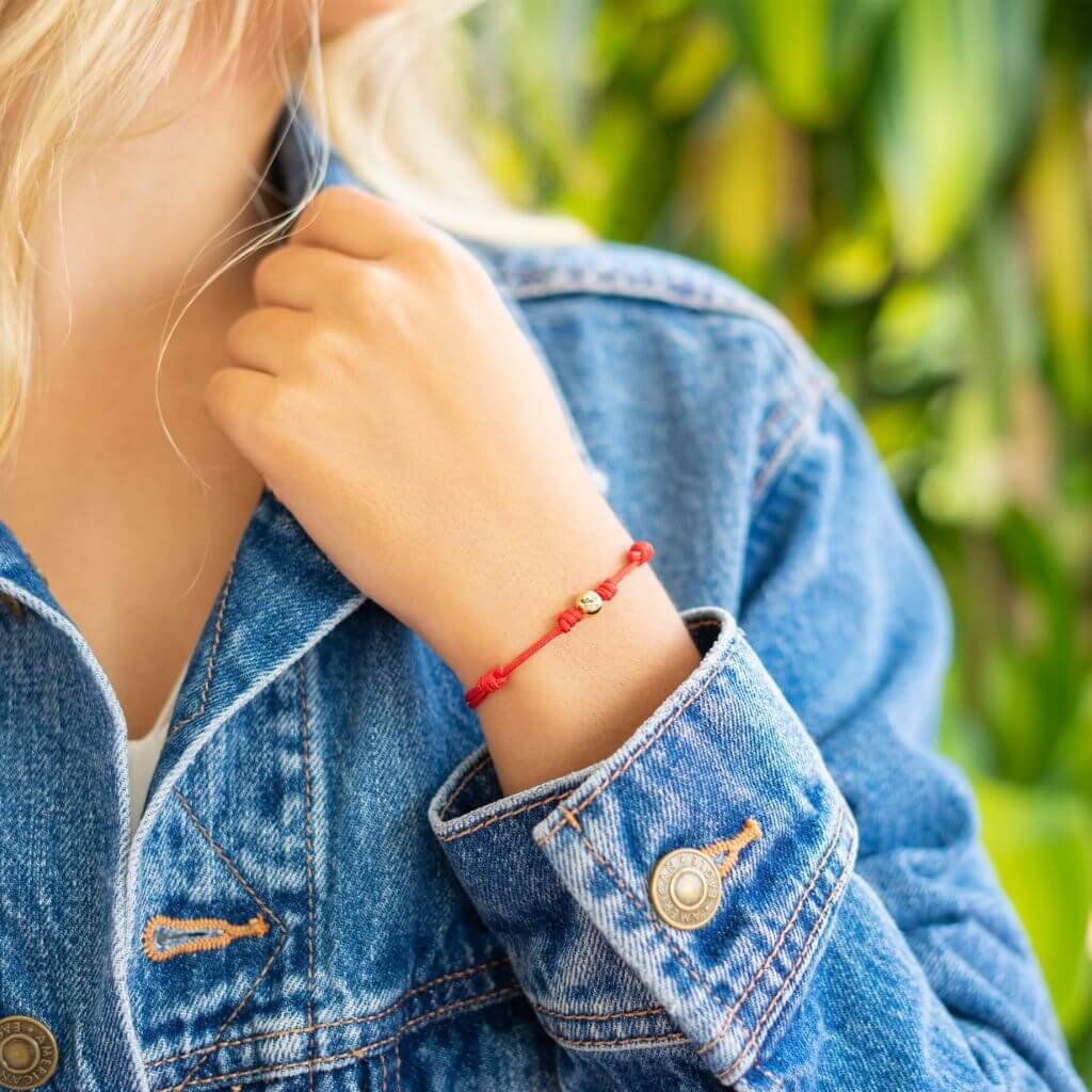 Woman fastening a red string bracelet with 14K yellow gold clasp - Luck Strings