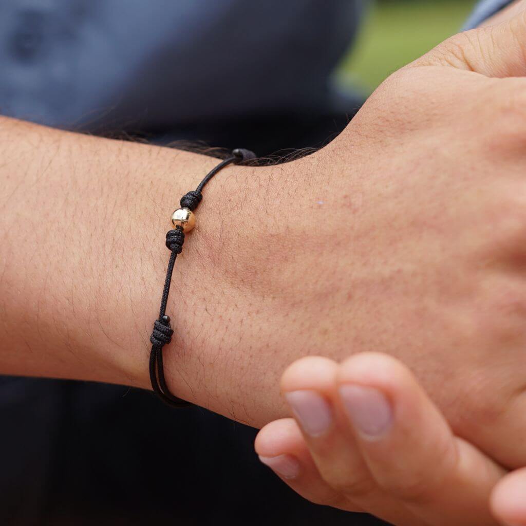 Man showcasing a black string bracelet with 14K yellow gold bead - Luck Strings