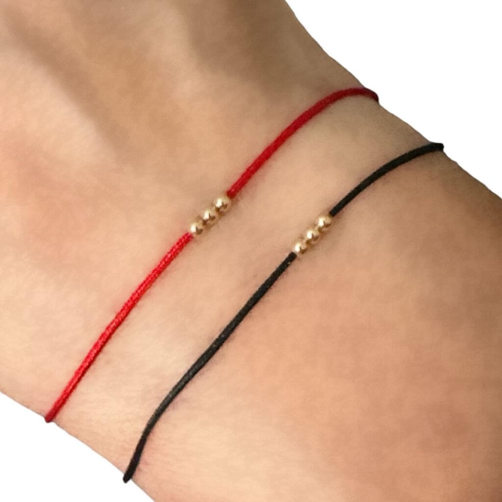 Luck Strings red and black string bracelet with 14k solid yellow gold triple beads on a person's wrist.