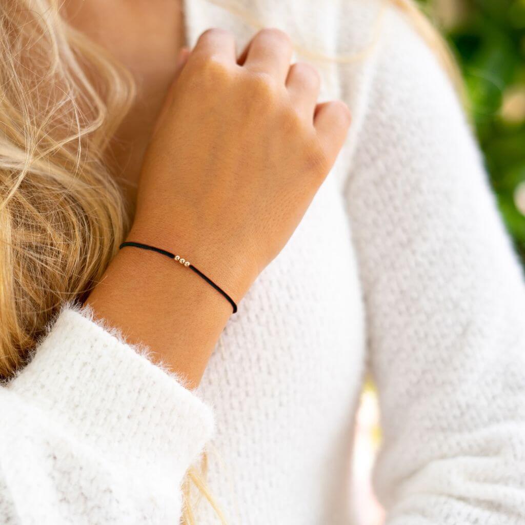 Luck Strings black string bracelet with 14k solid yellow gold triple beads on a person's wrist.