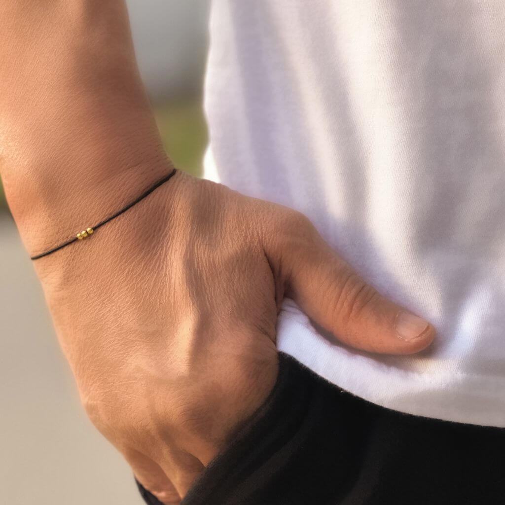 Luck Strings black string bracelet with 14k solid yellow gold triple beads on a person's wrist.
