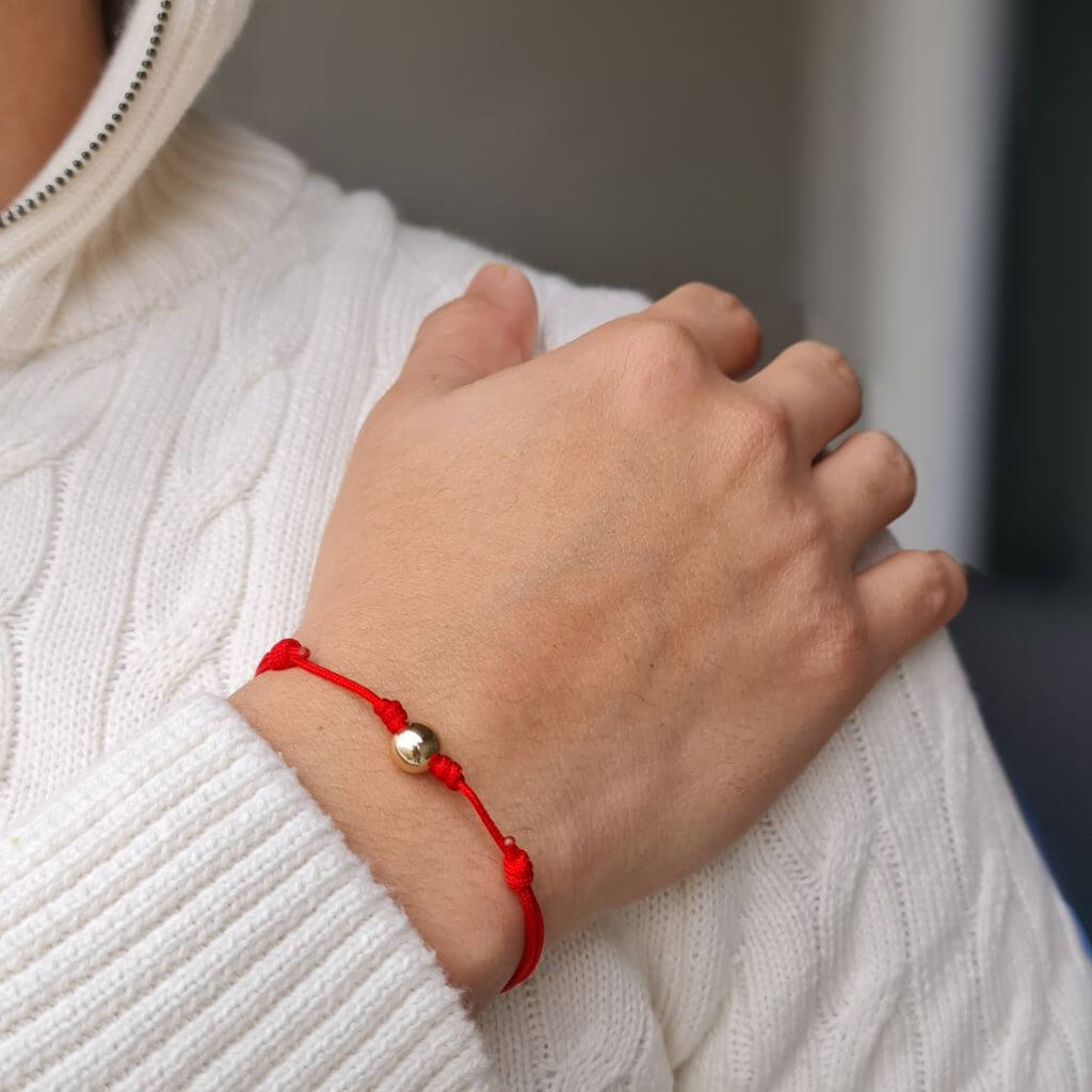 Man showcasing a red string bracelet with 14K yellow gold bead - Luck Strings