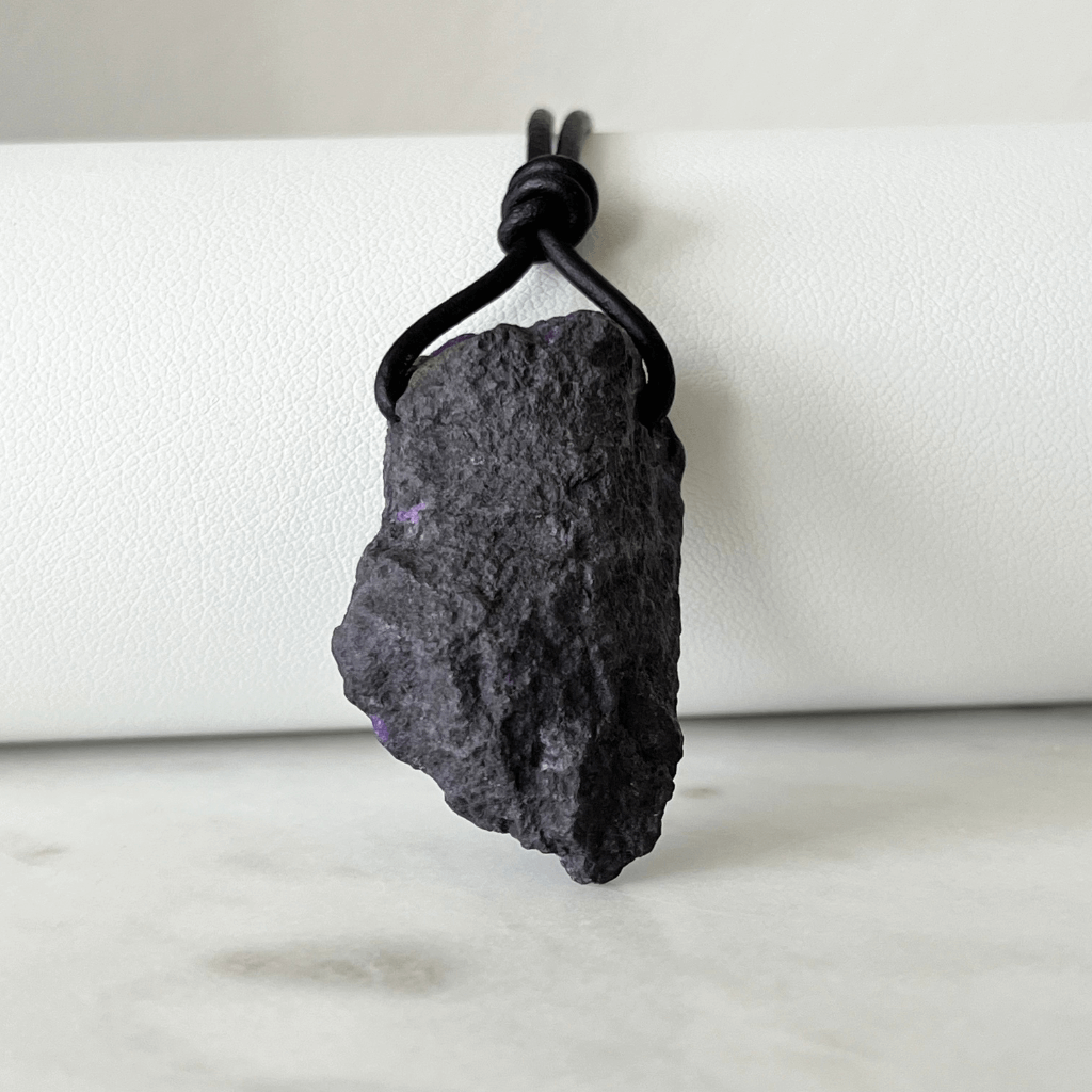 A one-of-a-kind Raw Sugilite Gemstone Pendant showcasing its distinctive deep purple color, suspended from a sleek cord, symbolizing spiritual growth and emotional healing - Luck Strings.