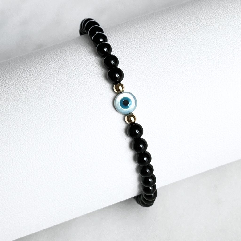 14K Gold and Black Tourmaline bracelet with Mother of Pearl evil eye on a wrist, highlighting the gold accents and snug fit - Luck Strings