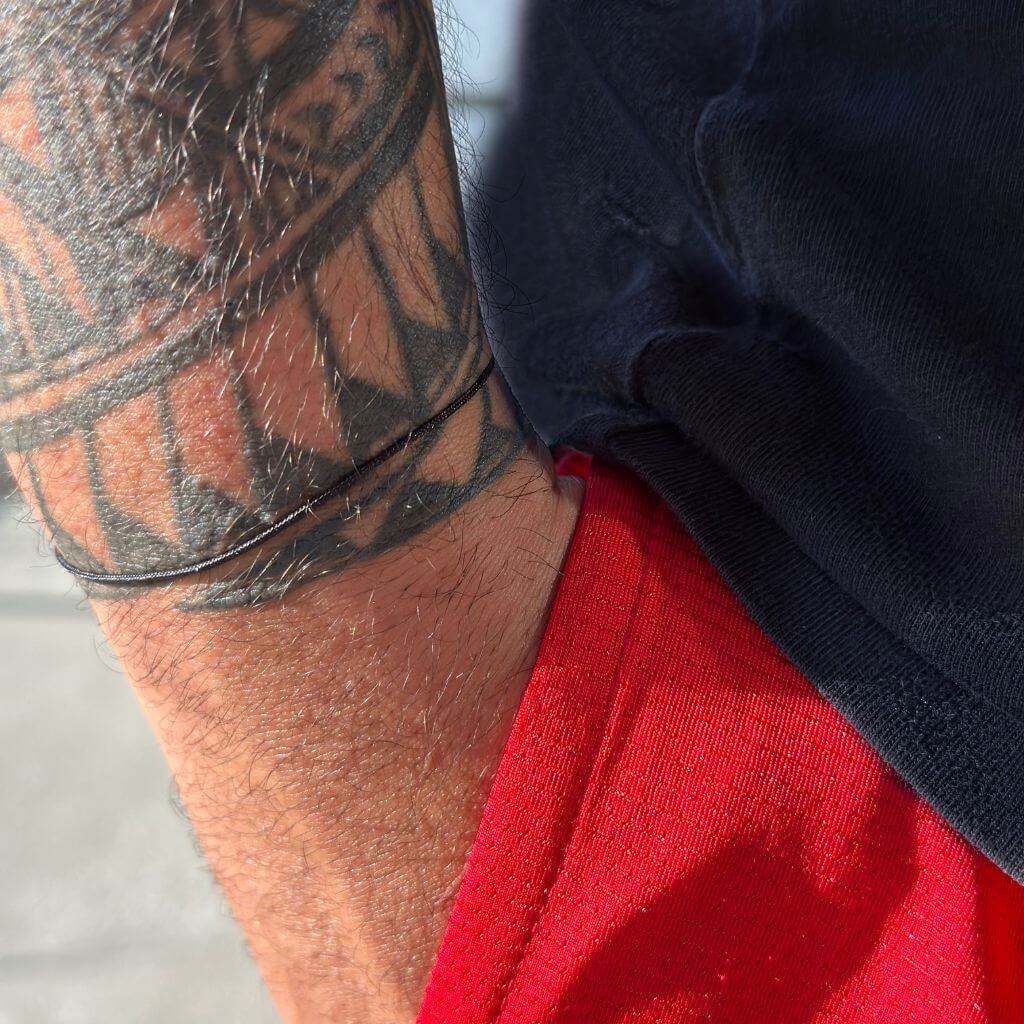 Man with tattooed arm wearing a black string bracelet, emphasizing its unisex and versatile design - Luck Strings