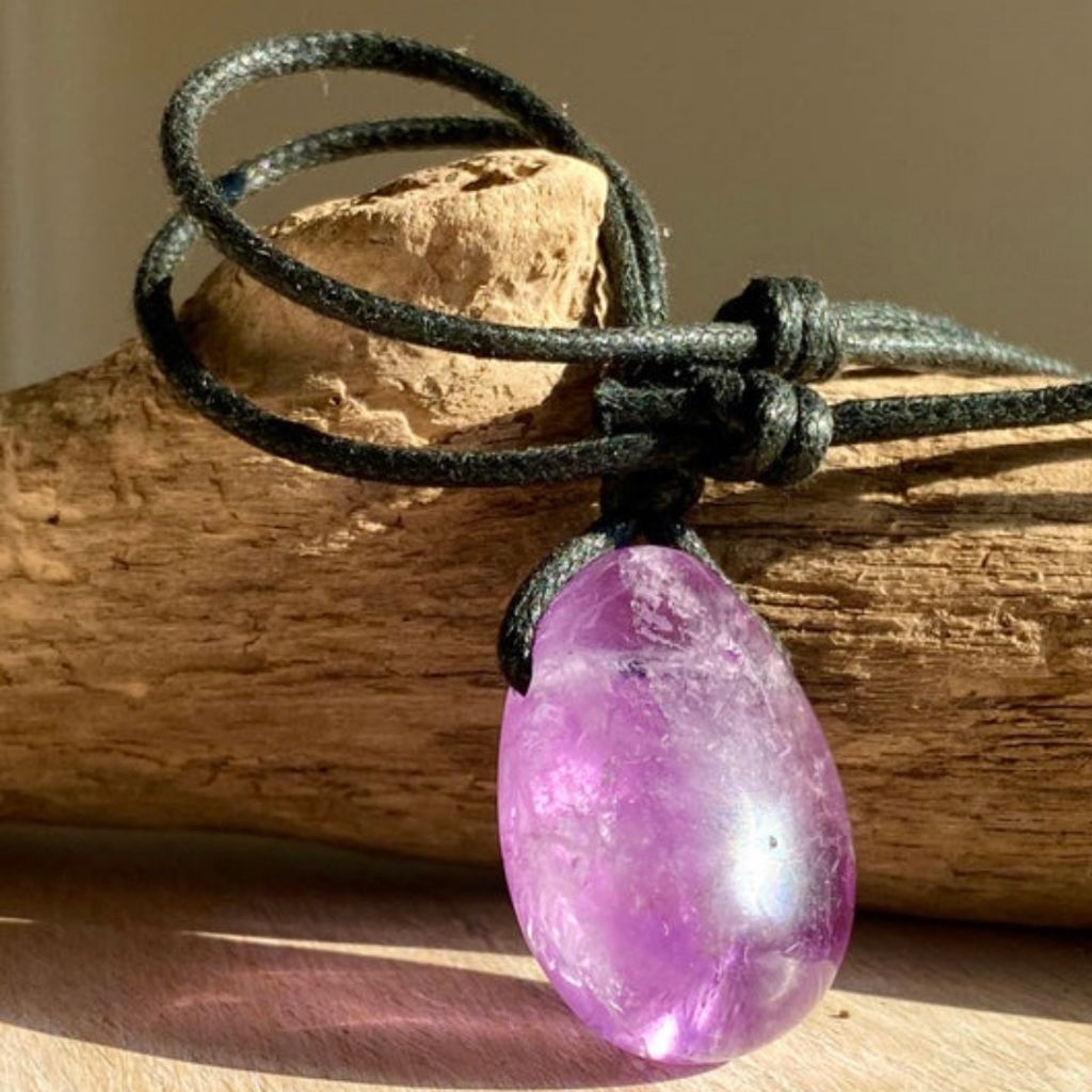 Luck Strings Amethyst pendant resting on a rustic wooden trunk, highlighting the natural beauty of the gemstone.