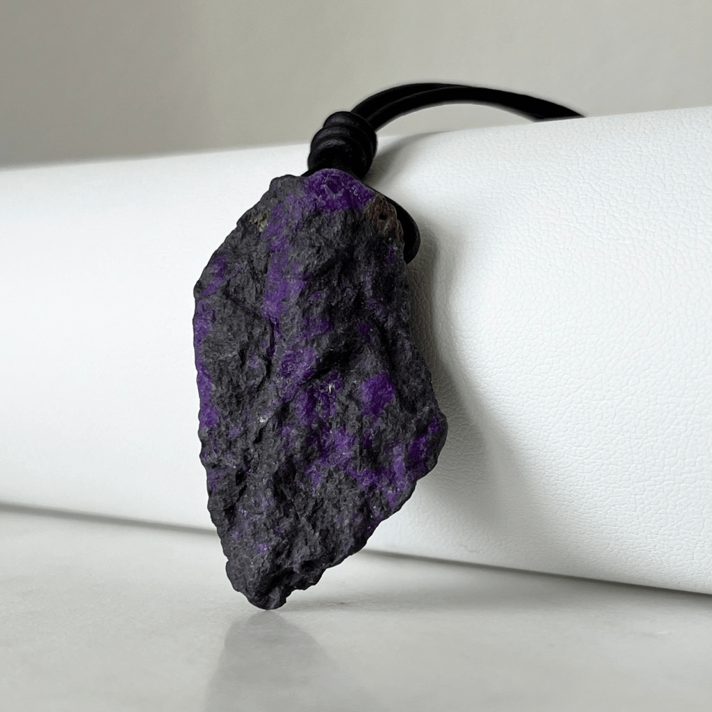 A one-of-a-kind Raw Sugilite Gemstone Pendant showcasing its distinctive deep purple color, suspended from a sleek cord, symbolizing spiritual growth and emotional healing - Luck Strings.