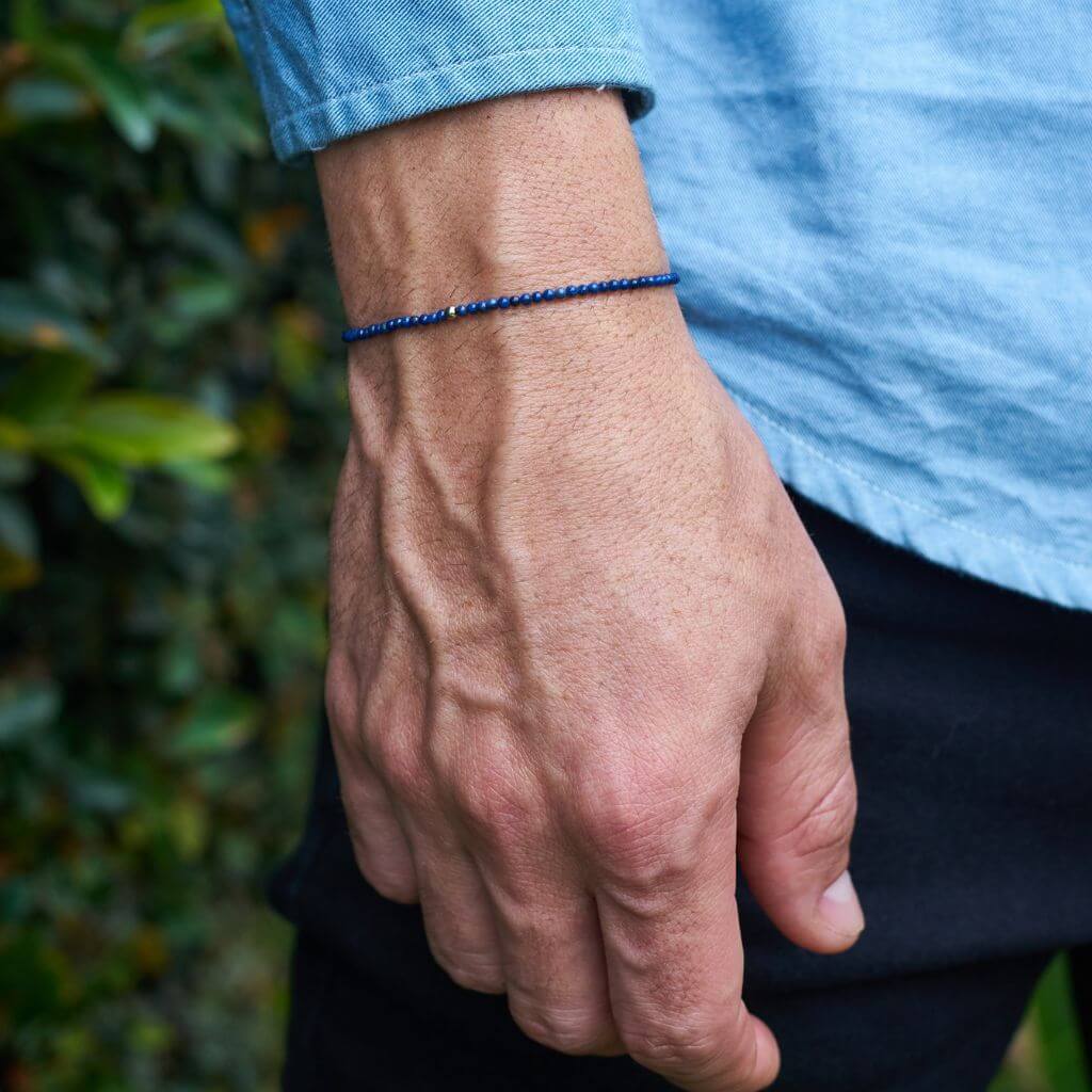 Man showcasing a Lapis Lazuli &amp; 14K Solid Gold Minimalist Bracelet on his wrist, highlighting the rich blue lapis against the luxurious gold - Luck Strings.