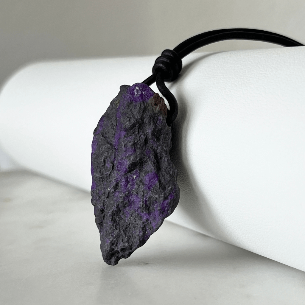 A one-of-a-kind Raw Sugilite Gemstone Pendant showcasing its distinctive deep purple color, suspended from a sleek cord, symbolizing spiritual growth and emotional healing - Luck Strings.