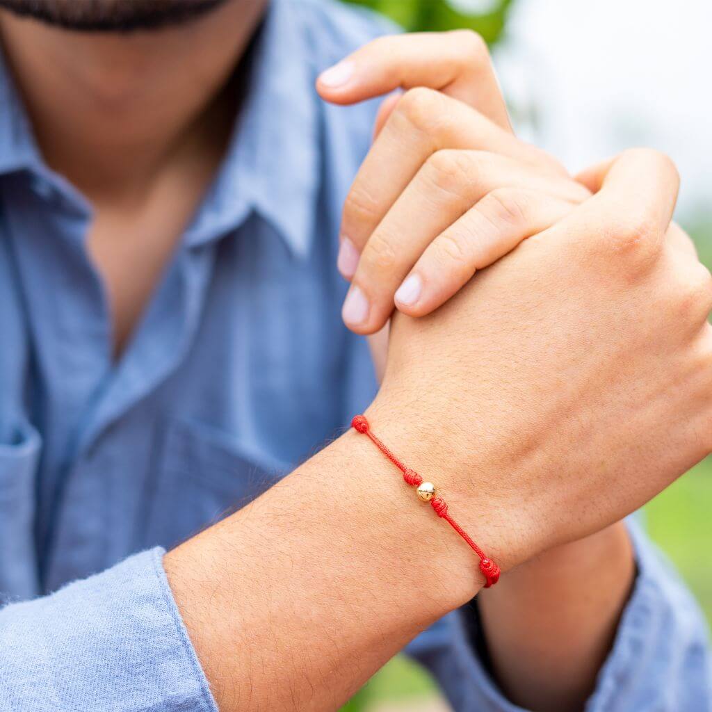 Man showcasing a red string bracelet with 14K yellow gold bead - Luck Strings