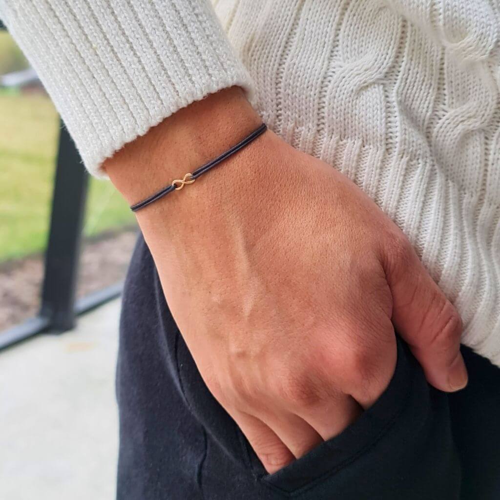 man with a Petite 14K Gold Infinity Bracelet from Luck Strings, demonstrating the bracelet's versatile and sophisticated appeal on his wrist.