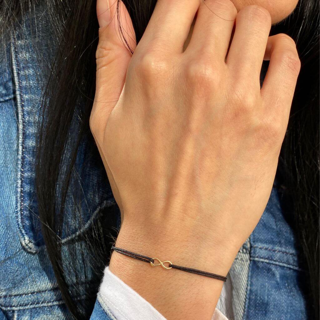 Elegant woman wearing a Petite 14K Gold Infinity Bracelet from Luck Strings, showcasing its delicate and timeless design on her wrist.
