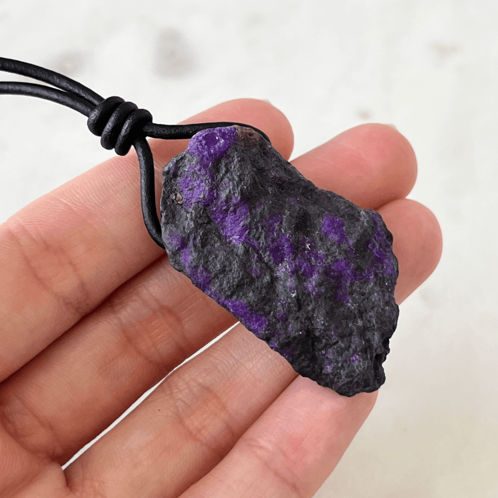 A one-of-a-kind Raw Sugilite Gemstone Pendant showcasing its distinctive deep purple color, suspended from a sleek cord, symbolizing spiritual growth and emotional healing - Luck Strings.