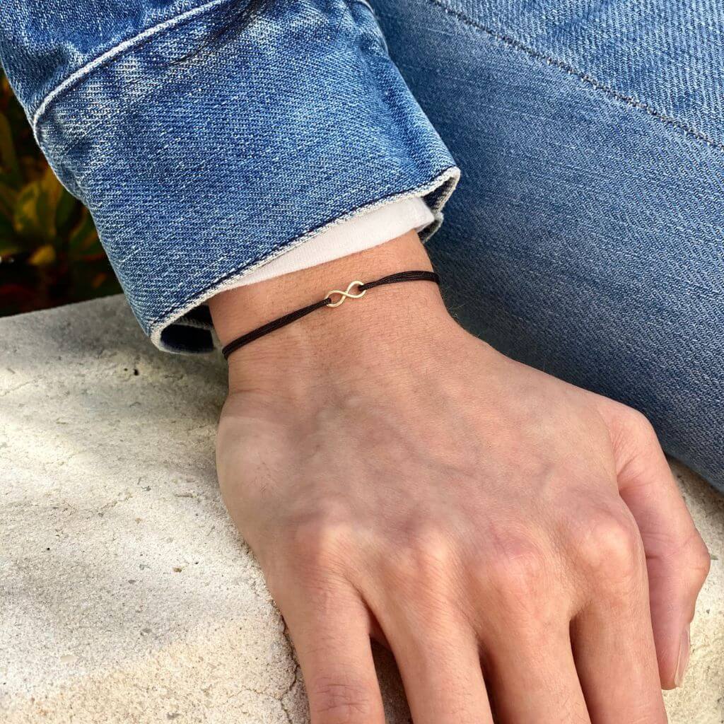 Elegant woman wearing a Petite 14K Gold Infinity Bracelet from Luck Strings, showcasing its delicate and timeless design on her wrist.