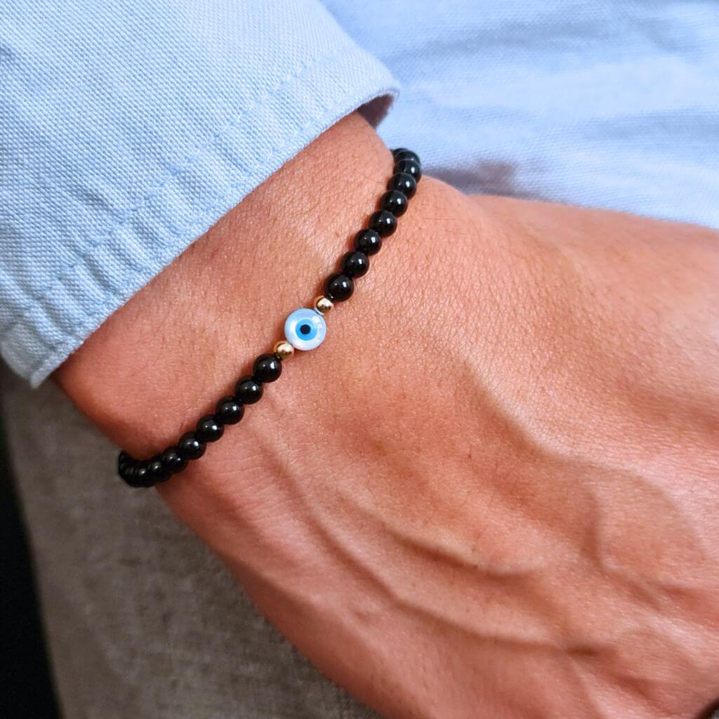 14K Gold and Black Tourmaline bracelet with Mother of Pearl evil eye on a wrist, highlighting the gold accents and snug fit - Luck Strings