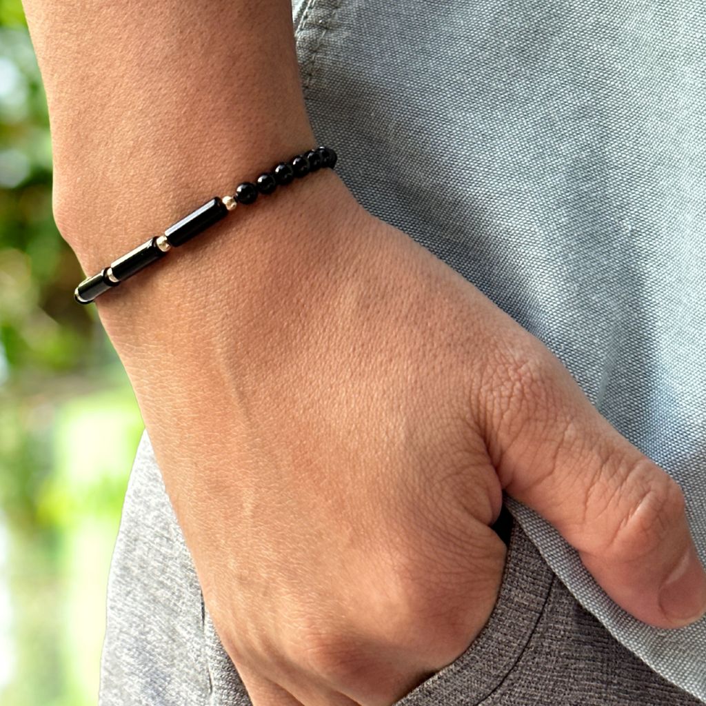 Man's wrist featuring the Black Tourmaline 14K Gold Bracelet, highlighting the sleek black gemstone beads complemented by gleaming gold accents - by Luck Strings.