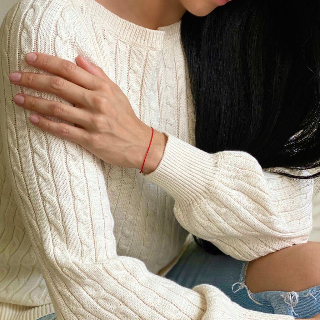 Women wearing a red string bracelet, symbolizing protection and spirituality, against a white sweater background - Luck Strings