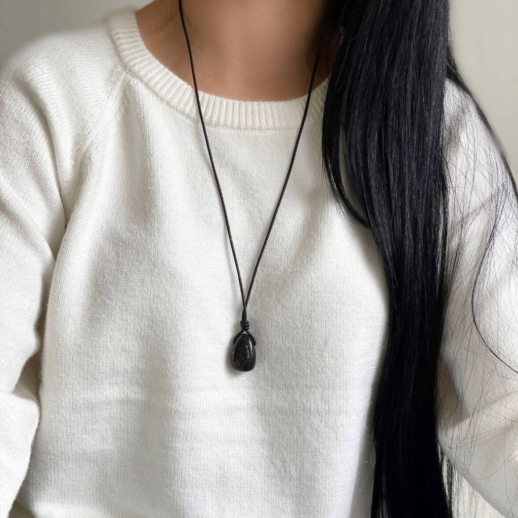 Woman wearing an adjustable necklace with a dark Nuummite gemstone pendant against a light sweater background, by Luck Strings