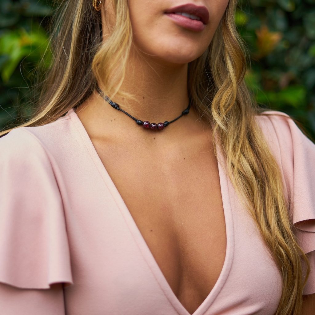 Luck Strings garnet beaded choker modeled against a soft pink blouse, highlighting the stones&#39; rich color.